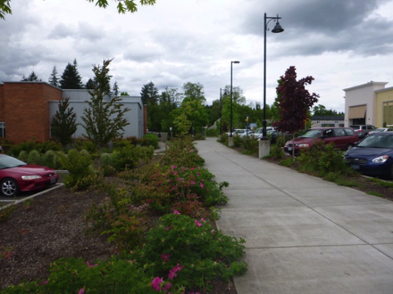 Sidewalk at Tualatin Public Library that leads to crosswalk at trail entrance - parking lot at mall